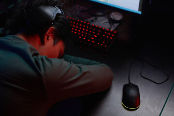 Rear view of young gamer in headphones sleeping at the table during game in dark room © AnnaStills