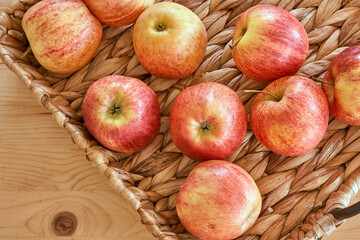 Ripe organic red and yellow apples lie in wicker tray on light wooden table. Autumn harvest. Top view.