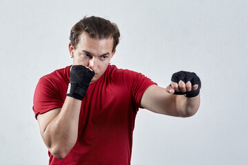 Young man boxes, making jab with left hand. Black bandages, red T-shirt, determined face...