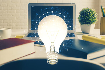 Computer on desktop in office with bulb icon hologram. Double exposure. Concept of idea.