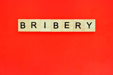 Word bribery. Wooden blocks with lettering on top of red background. Top view of wooden blocks with letters on red surface