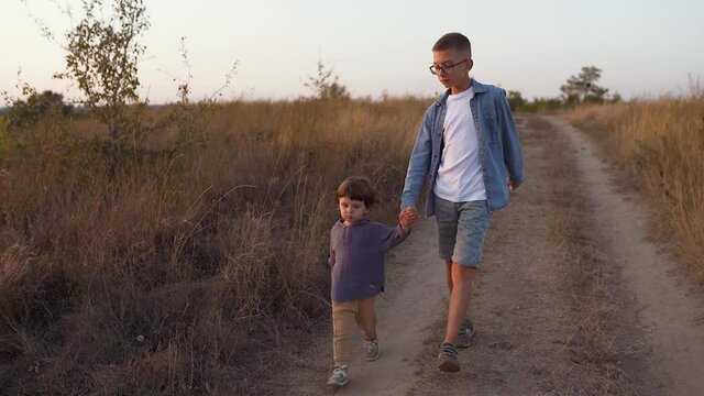 Toddler holding hand his big brother and walking at sunset