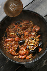 Close up of huge pan of home cooked delicious hot spicy seafood paella, traditional Spanish dish with rice, mussels, shrimps, prawns on rustic wooden background. Lifestyle edit. 