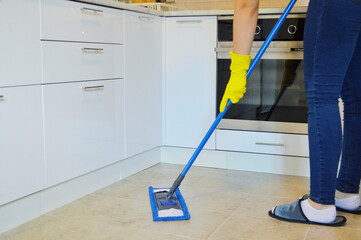 Young woman washing mop the tiled floor in the kitchen.