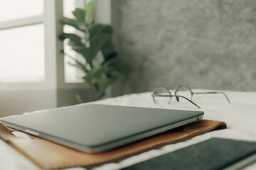 Working set of laptop smartphone and eyeglasses on white bed in bedroom.