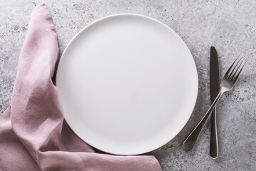 Empty ceramic plate white, napkin and cutlery on the table with concrete texture, top view. Food...