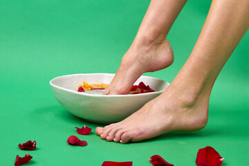Obraz na płótnie Canvas Woman's dipping her foot into aroma spa bowl. Taking herbal bath isolated on green background.