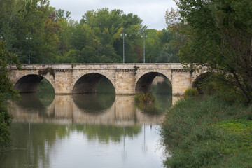 Fototapeta na wymiar ashlar stone medieval bridge, puente mayor, crossing rio carrion, in autumn. Palencia, Spain.