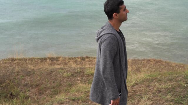 A man walking alone at the Black Sea coast in autumn. Media. Young woman with black hair walking on yellow grass of the hill along the sea and thinking about something.