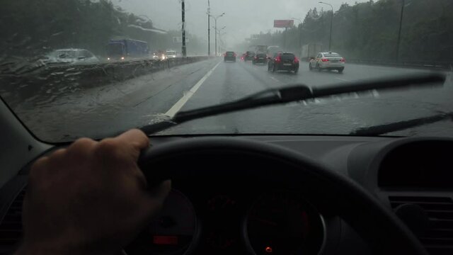 Man's hand drives a car on a rainy day in a heavy traffic, first-person view