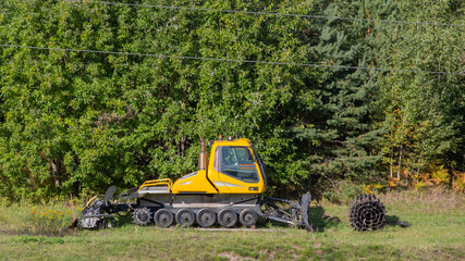 A yellow grader stands in the mountains in summer without caterpillars. Machine for driving on snow...