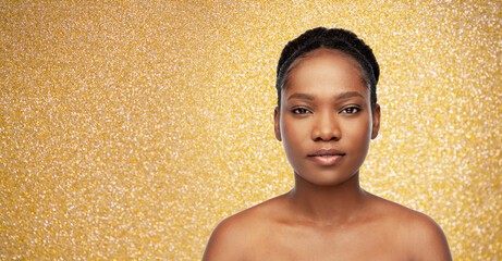 Obraz na płótnie Canvas beauty, luxury and people concept - portrait of young african american woman with bare shoulders over golden glitter on background