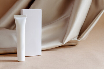 White tube of moisturizing luxury niche face cream gel with box on background of fabric drapery. Cosmetics products for personal care, hygiene concept. Minimalist packing, branding.