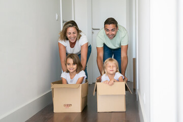 Caucasian mom and dad pushing cardboard boxes with kids inside. Happy parents and two daughters...
