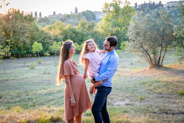 Young expecting parents with daughter standing in field