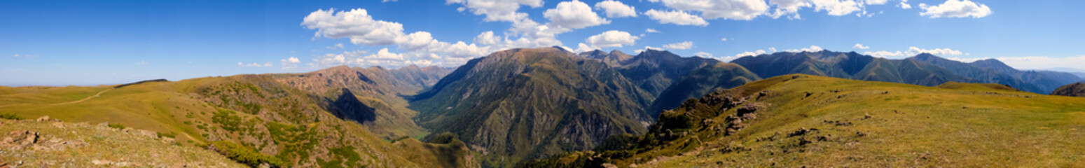 Naklejka premium Panorama of mountain gorge with cloudy blue sky. Summer nature landscape. River valley panorama. Kora river gorge in Kazakhstan, way to Burkhan bulak waterfall. Tourism in Kazakhstan concept.