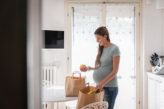 Happy pregnant woman with fresh groceries in kitchen