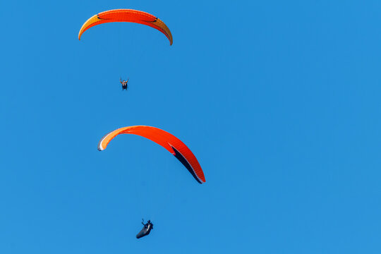 two people fly on a paraglider against a blue sky on a summer day