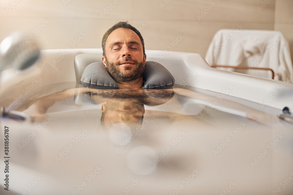 Wall mural bearded young man taking bath in spa salon