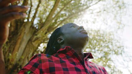 African man takes a big breath rises hands and look up a the sky. Sun rays comming through the tree. Hope and prayer concept. High quality photo