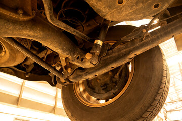 Under old car closeup rear wheel axle suspension and exhaust chamber silencer muffler dirty fix...