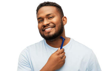 grooming and people concept - smiling young african american man shaving beard with manual razor blade over white background