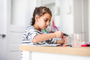 Naklejka premium Cropped shot of a focused little girl making a picture using different types of art supplies while being seated at a table inside during the day