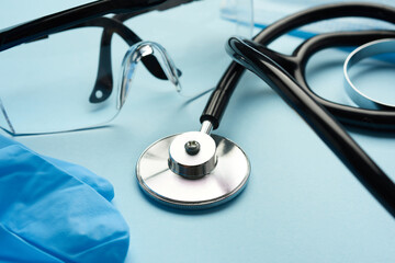 black medical stethoscope, plastic safety goggles on blue background