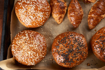 baked croissants and round buns with sesame seeds on an iron baking sheet with rolled brown baking paper