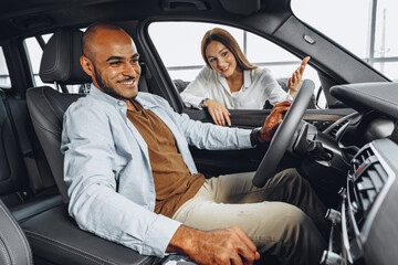 Young attractive woman salesperson in car showroom showing a car to her male client