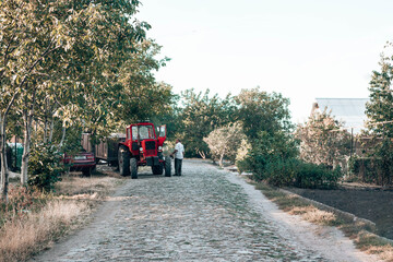 Red tractor stands by the road in the countryside. A man with a foot stands near a tractor