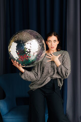 Naklejka premium Beautiful young woman in grey sweater and disco ball at home