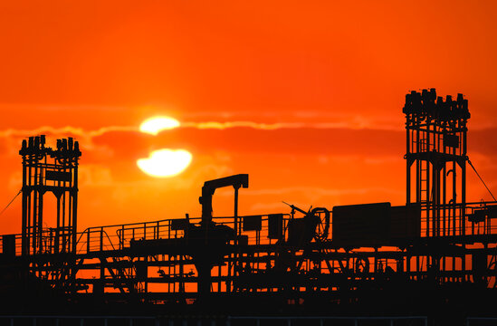 Silhouette pipelines system on crude oil tanker at harbor with blurred sunset sky background