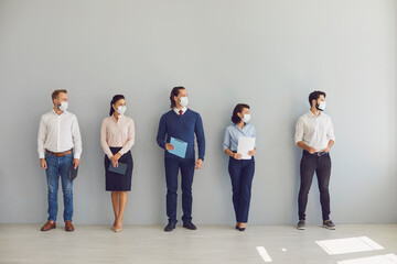 Obraz premium Job seekers in face masks waiting for job interview standing in corridor keeping safe distance