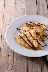 Sweet crepes with chocolate on wooden table. 	
