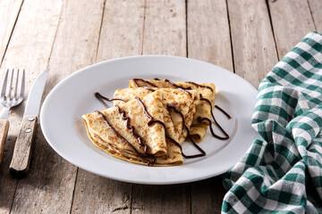Sweet crepes with chocolate on wooden table. 	