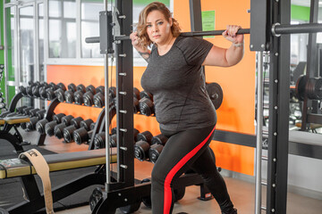 Fat woman fights overweight in the gym, doing heavy fitness exercises for future strong body. Obese person workout with sport equipment