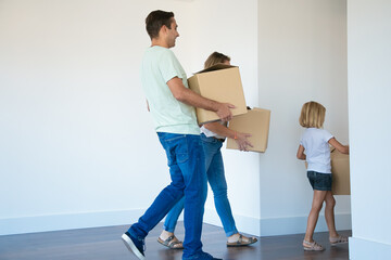Father holding cardboard box and going to corridor after wife and daughter. Cheerful young family...