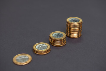 Stacks of golden and silver coins (1 Real) as in a growing graph, representing rise or fall on black bacground. Economy concept. Copy space. Selective focus. Brazilian coins
