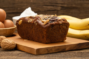 Close up Banana cakes are placed on a wooden tray on a wooden table, with bananas, eggs, flour as background.