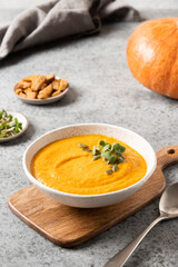 Pumpkin soup with cream on grey background. Vertical format.