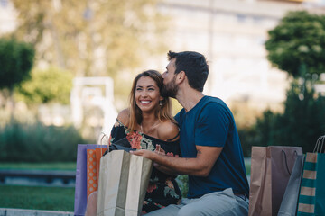 Young attractive couple in love sitting on the bench after shopping and talking. Woman bought a gift to her boyfriend.