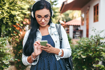 young beautiful stylish woman using smartphone, headphones, eye glasses, summer, vintage denim...