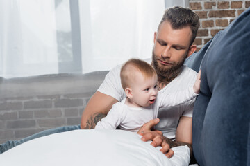 Obraz premium selective focus of young bearded man sitting on bed near infant child