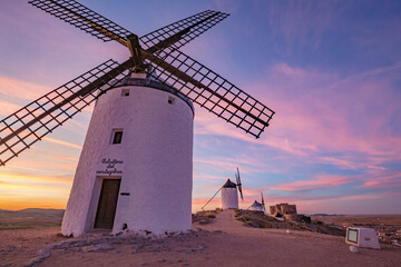 Beautiful white spanish windmill on the hill at fairy blue pink gold sunset near the castle in Consuegra, Toledo province, Spain - obrazy, fototapety, plakaty