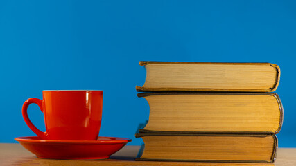 red cup with coffee and three old books lie on an oak table.