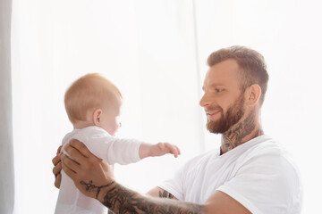 joyful young father holding infant son in baby romper