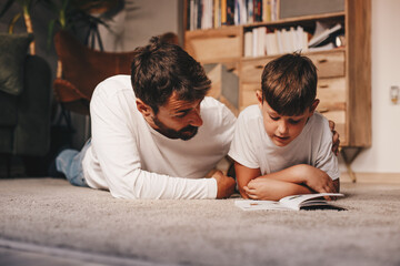 Young attractive father lying down on the floor with his son and studying with him.