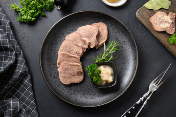 Beef tongue served horseradish sauce and rosemary sprig on black table. Juicy tender meat a great appetizer. Top view.