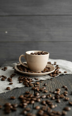 Coffee cup filled of fresh arabica or robusta coffee beans with scattered coffee beans on a linen textile and wood table.